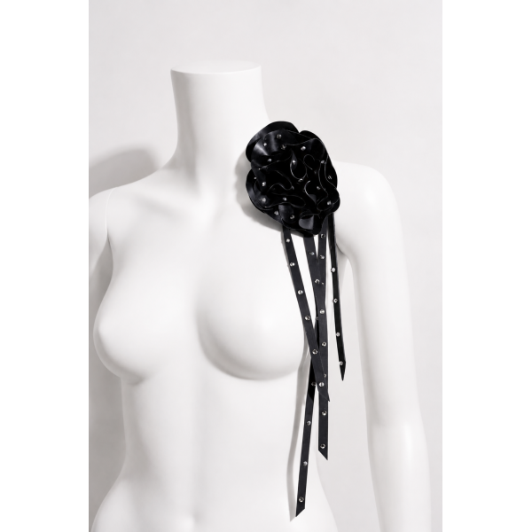 Latex Fashion by Vex A white mannequin torso displays a large black flower-shaped accessory with long, studded ribbon-like strands draping over its shoulder.